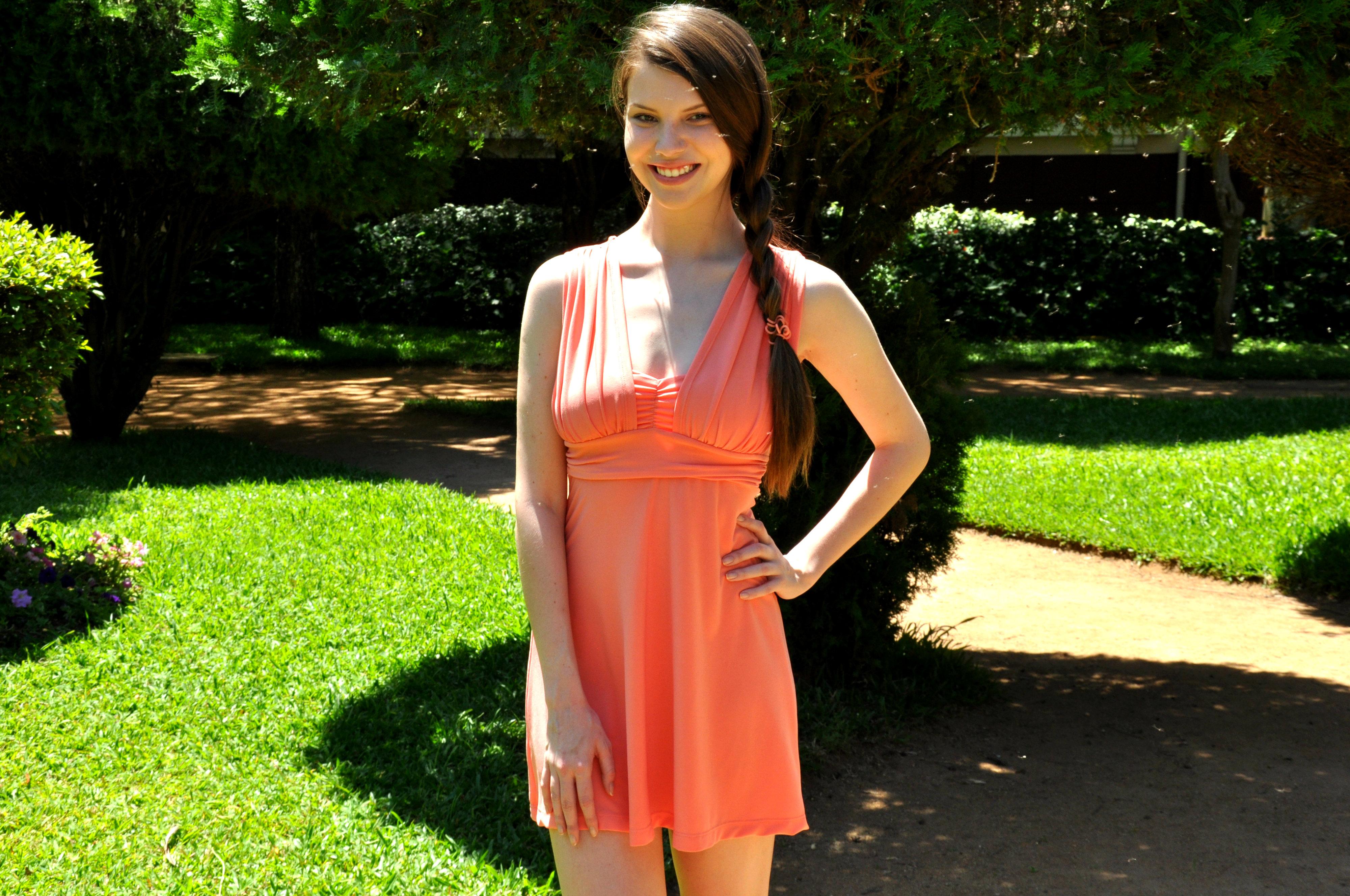 Mulher em vestido coral de verão em pé em jardim com fundo verde vibrante.