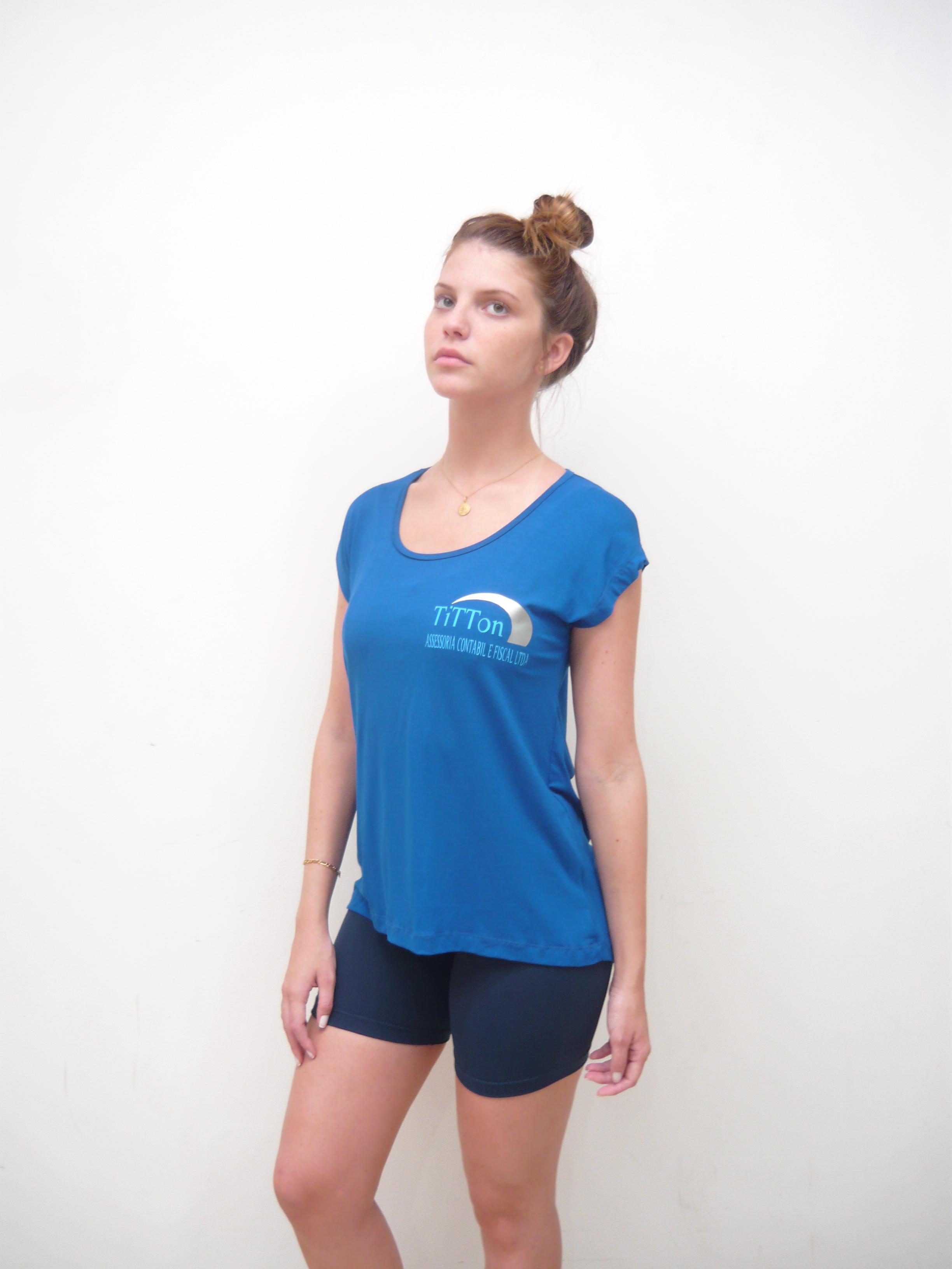 Mulher vestindo camiseta azul corporativa com logo Titton e shorts em ambiente profissional com fundo neutro.